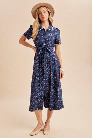 woman wearing a navy blue button-up midi dress with a tie waist and floral print, styled with a wide-brimmed hat