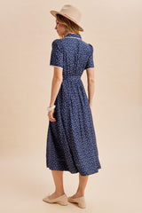 woman wearing a navy blue floral midi dress with short puff sleeves and a fitted waist, accessorized with a hat