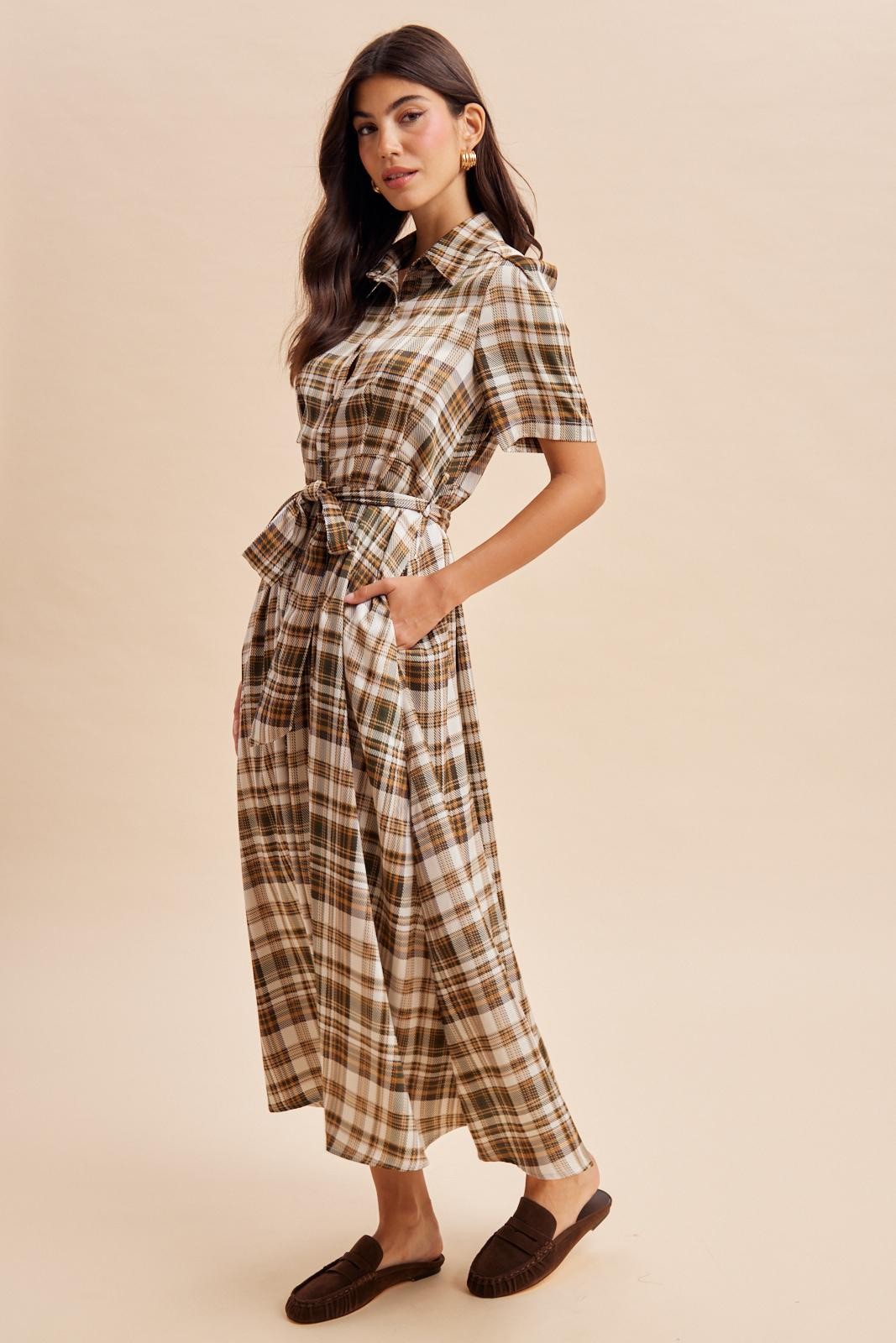 woman wearing a brown and white plaid shirt dress with a belted waist and pockets, standing on a neutral background