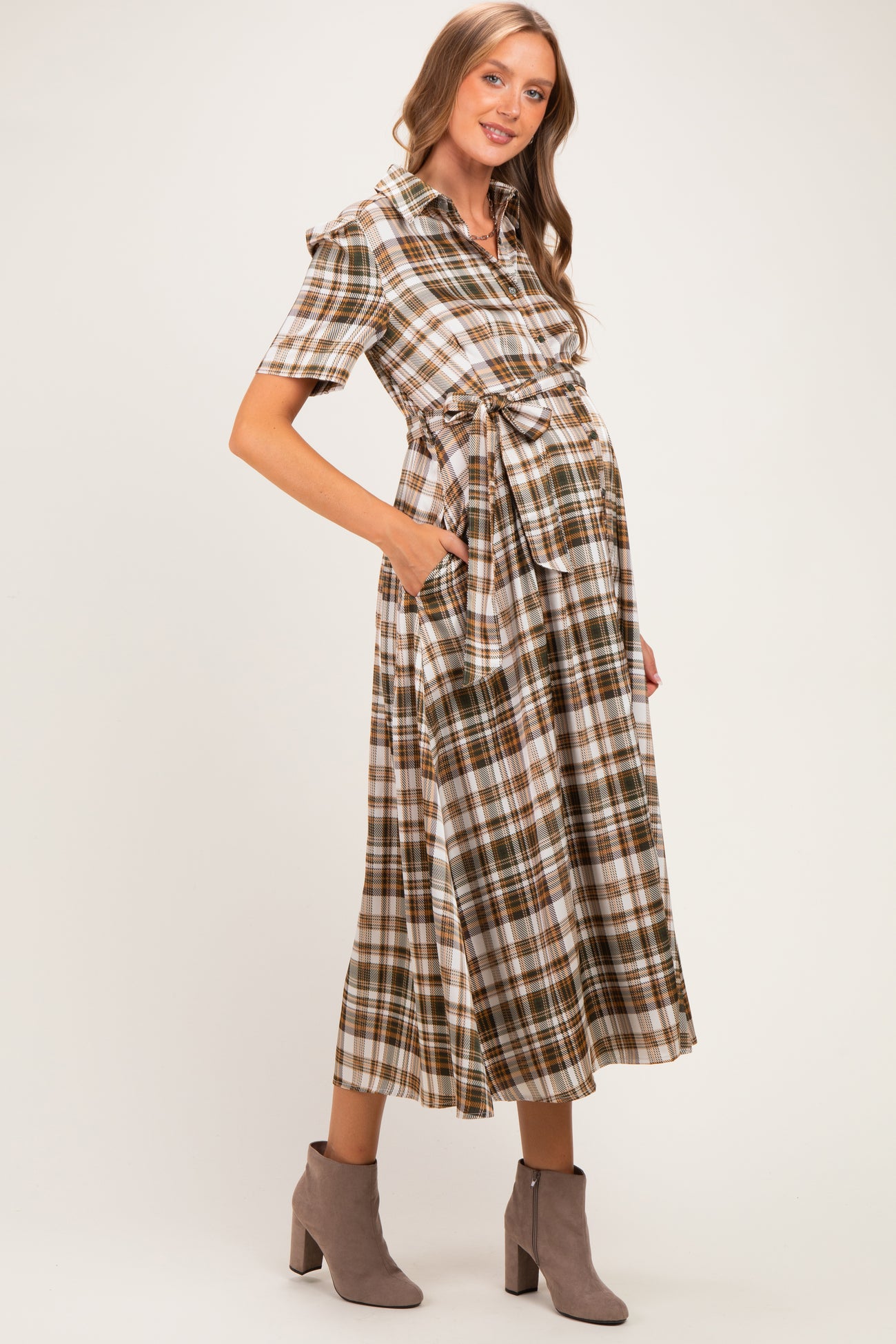 woman wearing a brown and white plaid maternity dress with a tie waist and pockets, showing her baby bump