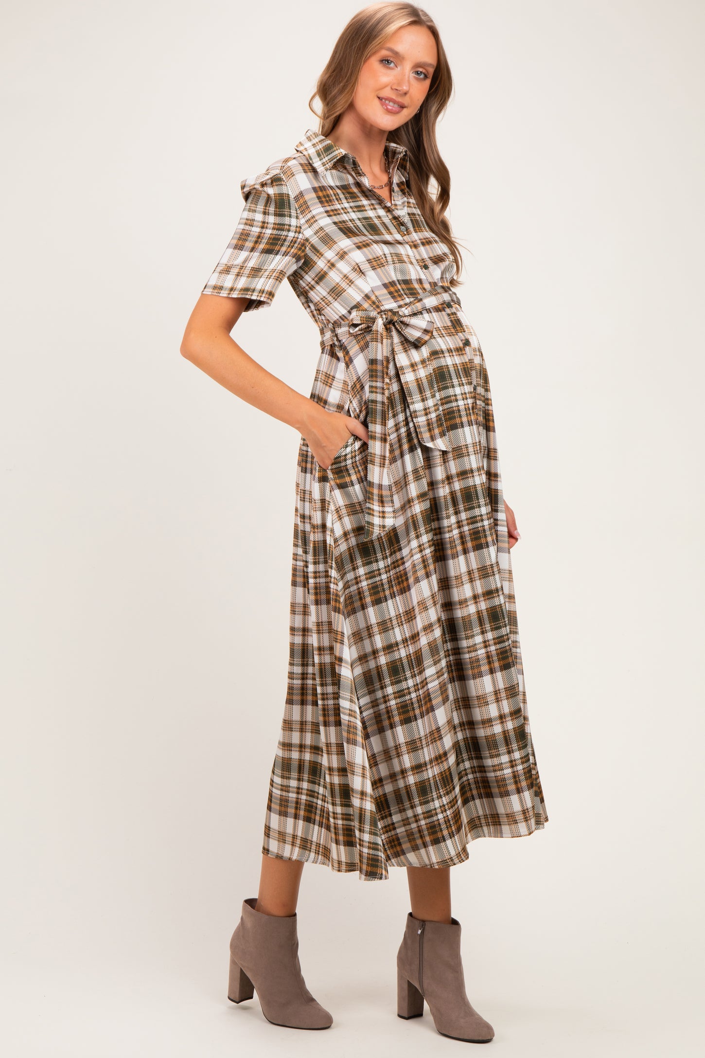 woman wearing a brown and white plaid maternity dress with a tie waist and pockets, showing her baby bump
