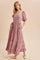 woman wearing a mauve puff sleeve maxi dress with floral pattern and pockets, standing against a neutral background