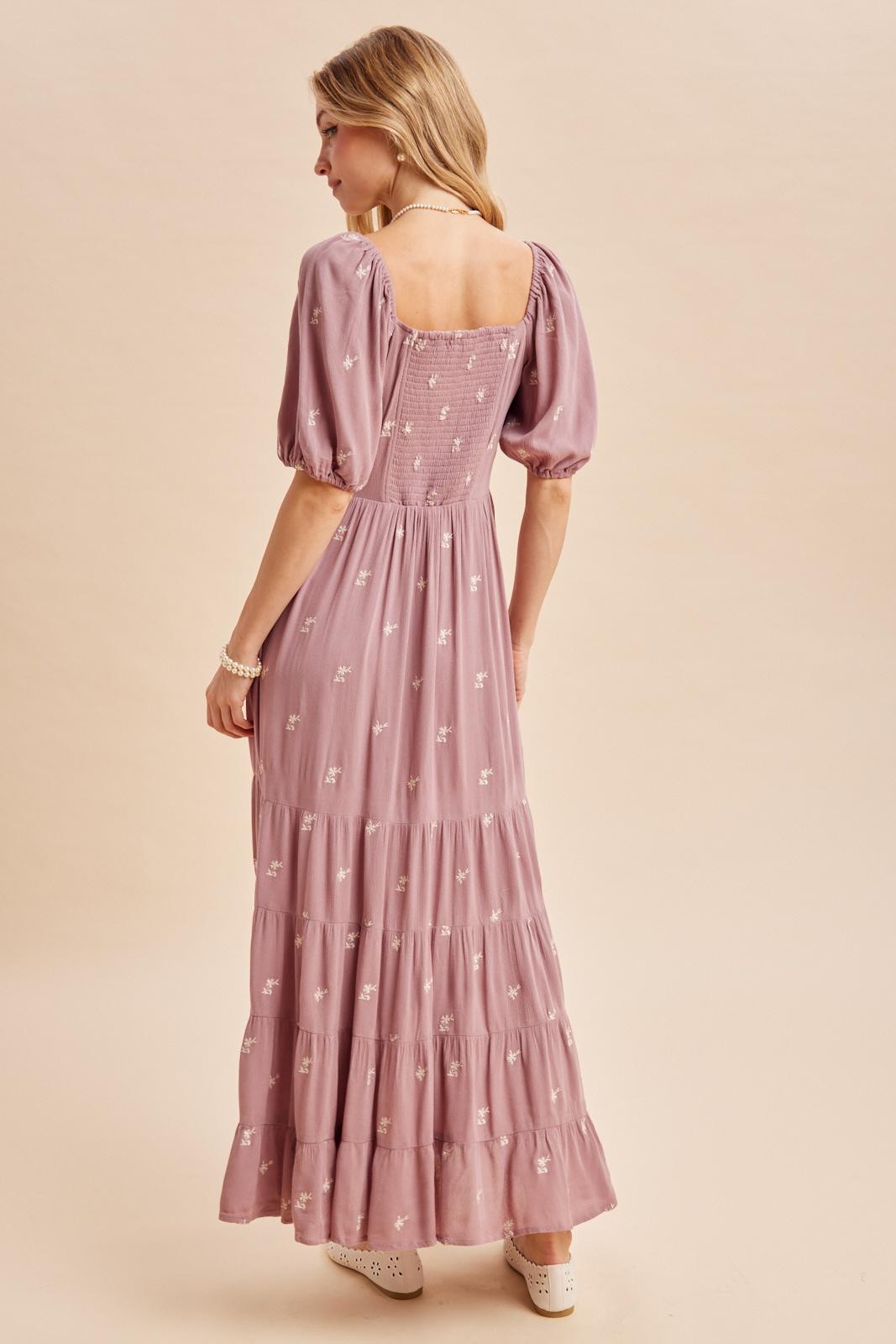 woman wearing a lilac maxi dress with puff sleeves and floral embroidery, showing the back view