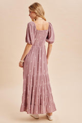 woman wearing a lilac maxi dress with puff sleeves and floral embroidery, showing the back view
