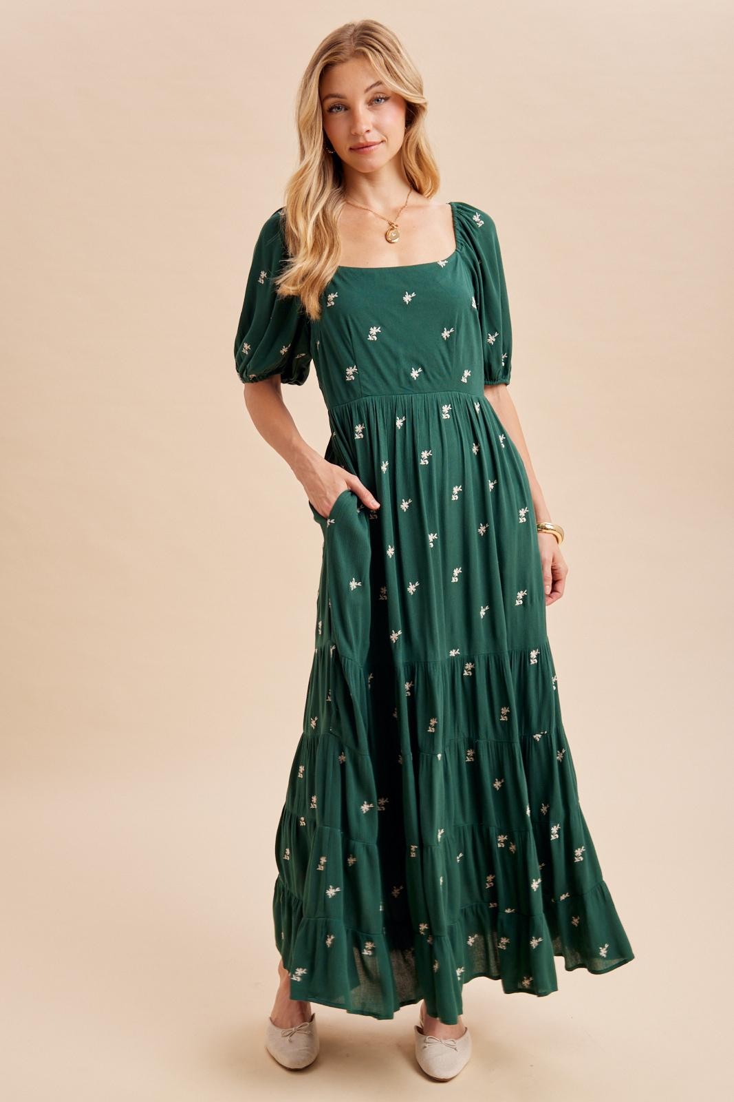 woman wearing a green maxi dress with puff sleeves and floral embroidery, styled with pockets and a flowing silhouette