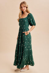 woman wearing a green floral maxi dress with puff sleeves and pockets, standing on a neutral background