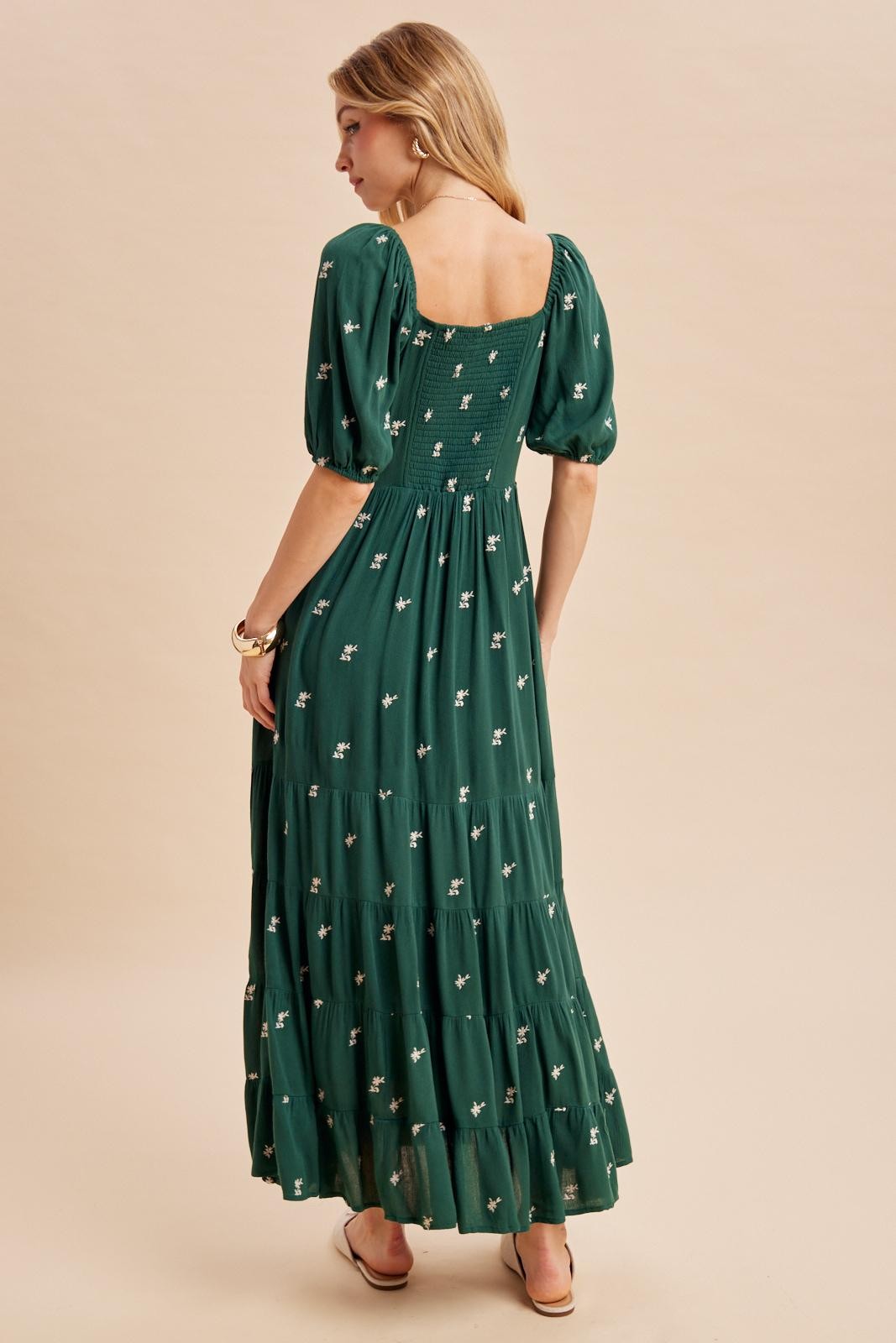 woman wearing a green maxi dress with puff sleeves and floral embroidery, showing the back design