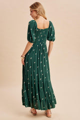 woman wearing a green maxi dress with puff sleeves and floral embroidery, showing the back design