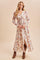 woman wearing a floral maxi dress with long sleeves and a tie waist, paired with brown ankle boots