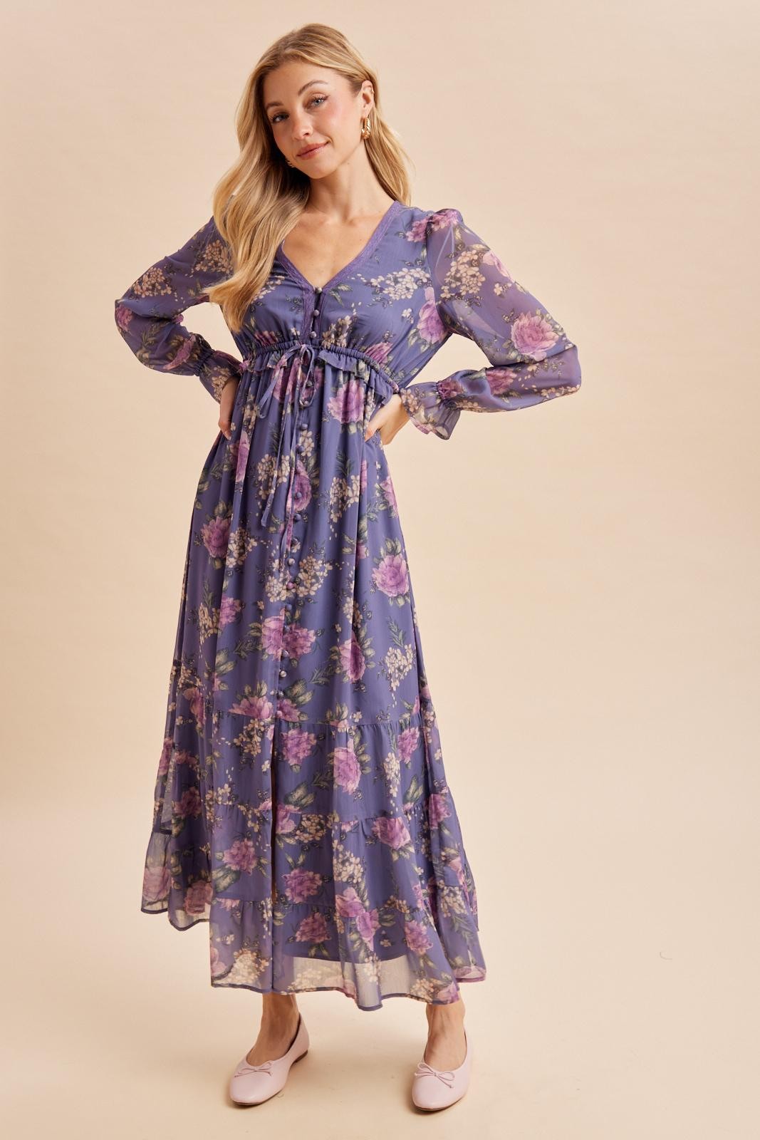 woman wearing a purple floral maxi dress with long sleeves and a tie waist detail