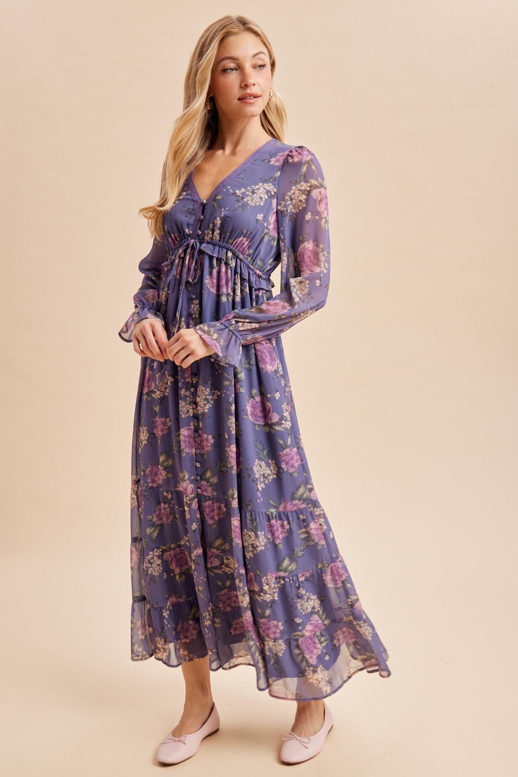 woman wearing a flowy purple floral maxi dress with long sleeves and a cinched waist, paired with pink flats