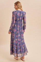 woman wearing a long sleeve purple floral maxi dress with a ruffled hem and waist detail, viewed from the back