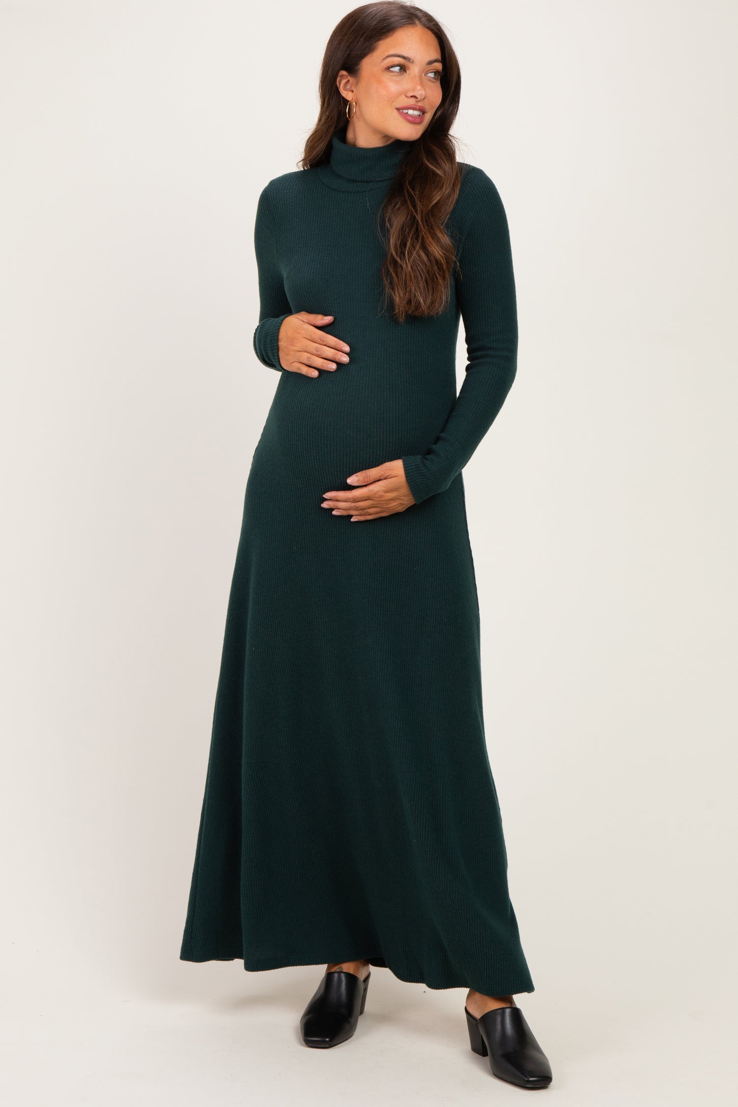 woman wearing a dark green long sleeve maternity maxi dress while holding her baby bump