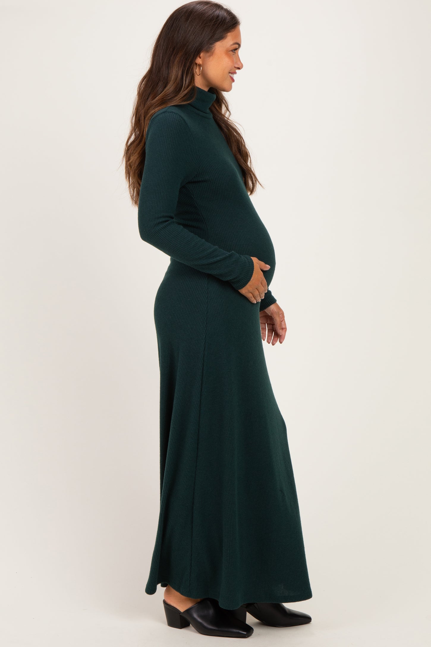 woman wearing a dark green long sleeve maternity dress with a fitted turtleneck and baby bump visible
