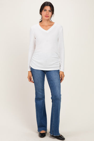 woman wearing a white long sleeve v-neck top with ruched sides and blue flared jeans