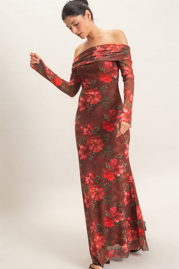 woman wearing a floral off-shoulder long sleeve gown in red and brown colors, posing with one hand raised