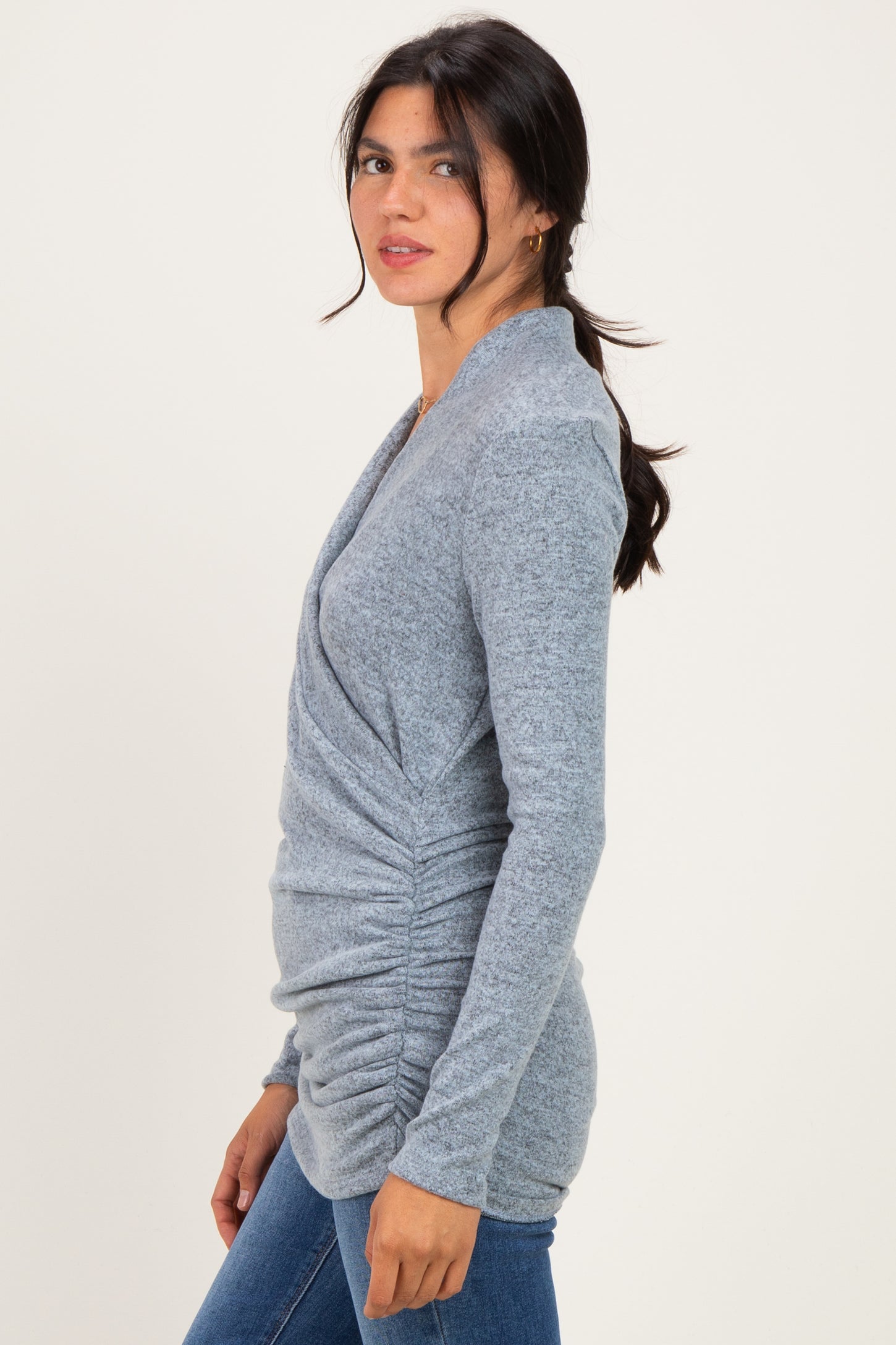 woman wearing a gray long sleeve shirt with gathered detailing and a relaxed fit, styled with blue jeans