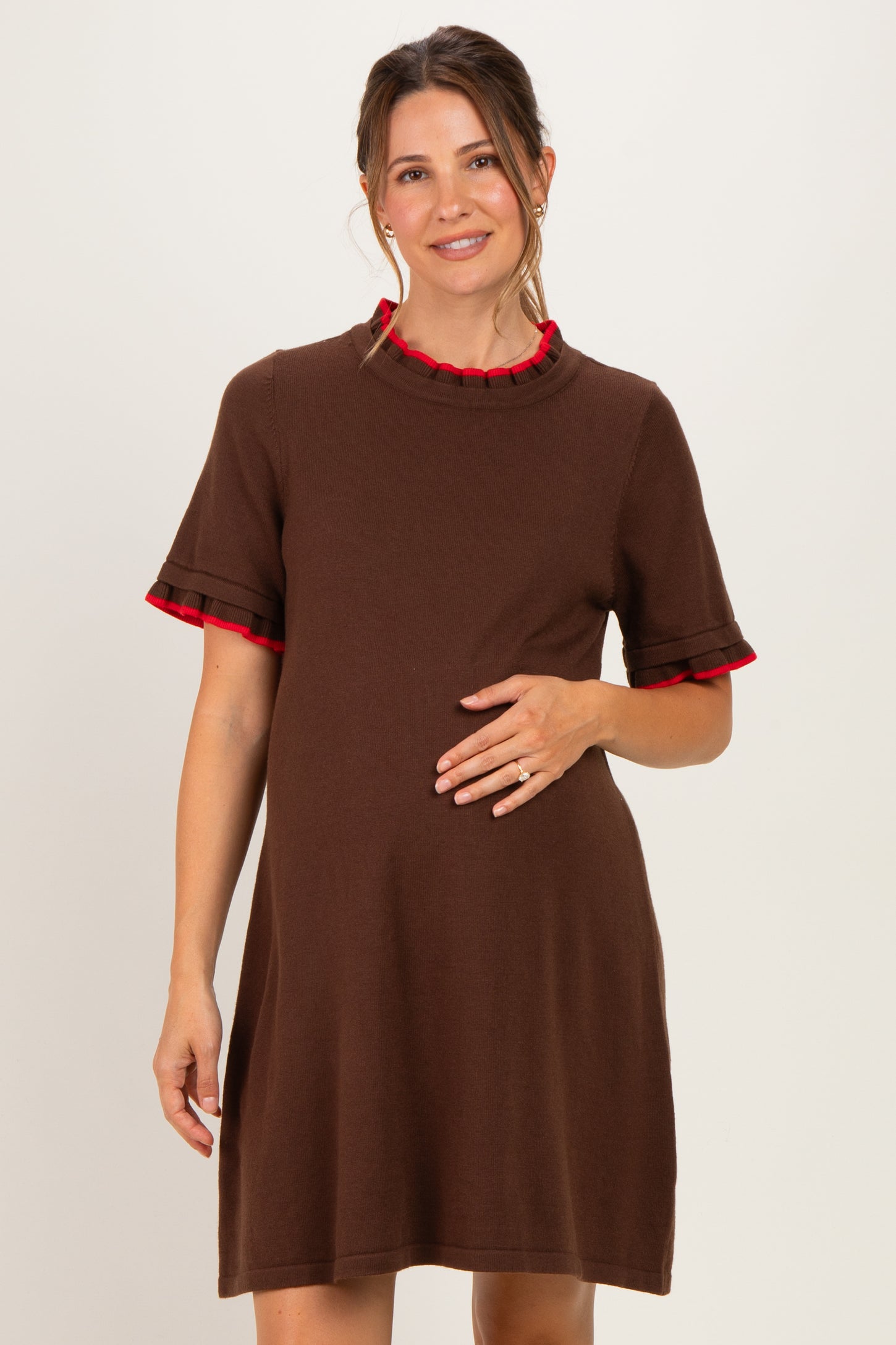 woman wearing a brown short sleeve maternity dress with red ruffle details and holding her baby bump