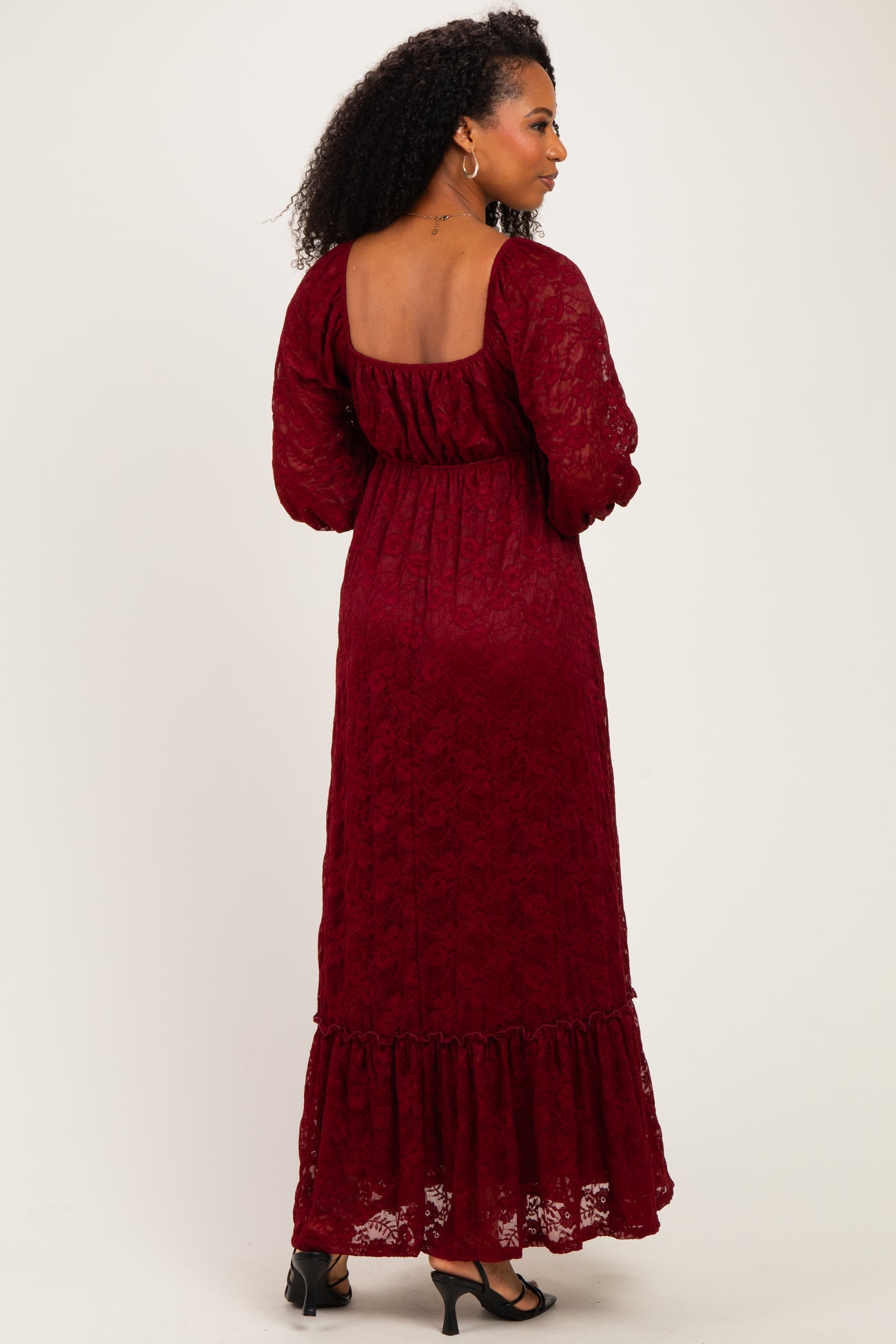 woman wearing a burgundy lace maxi dress with long sleeves and a ruffled hem, viewed from the back