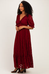 woman wearing a burgundy lace maxi dress with puff sleeves and a tie detail at the neckline