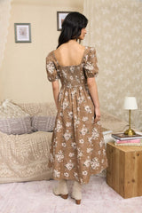 woman wearing a brown floral maxi dress with puff sleeves and a smocked back, standing in a cozy room