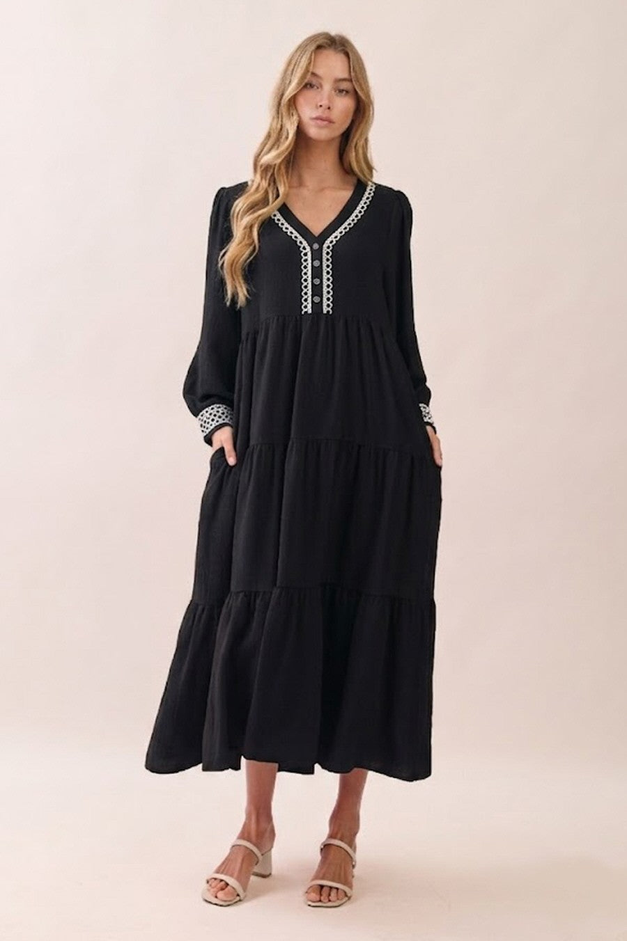woman wearing a black tiered maxi dress with long sleeves and decorative detailing on the neckline and cuffs