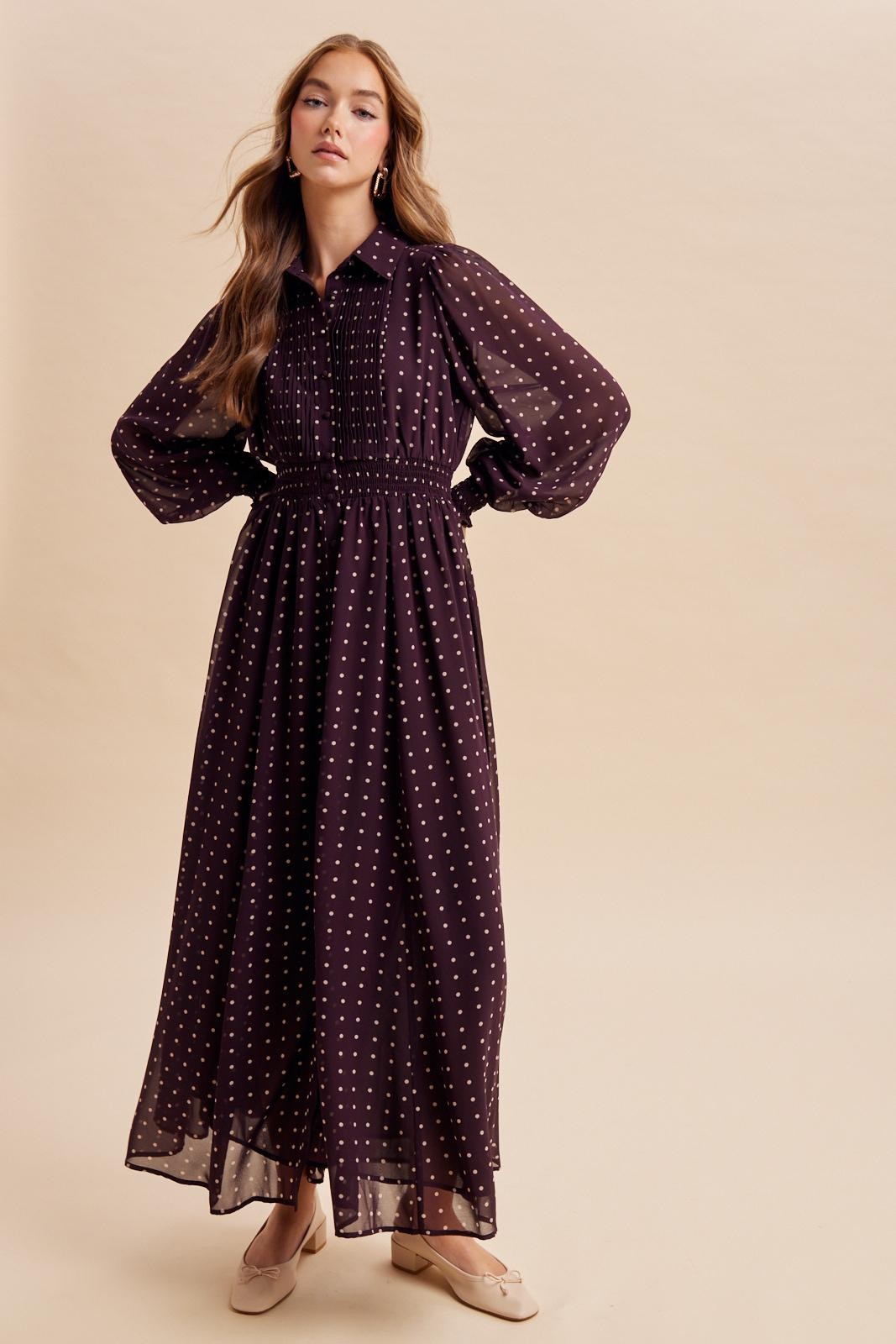 woman wearing a long burgundy polka dot maxi dress with a smocked waist and puff sleeves