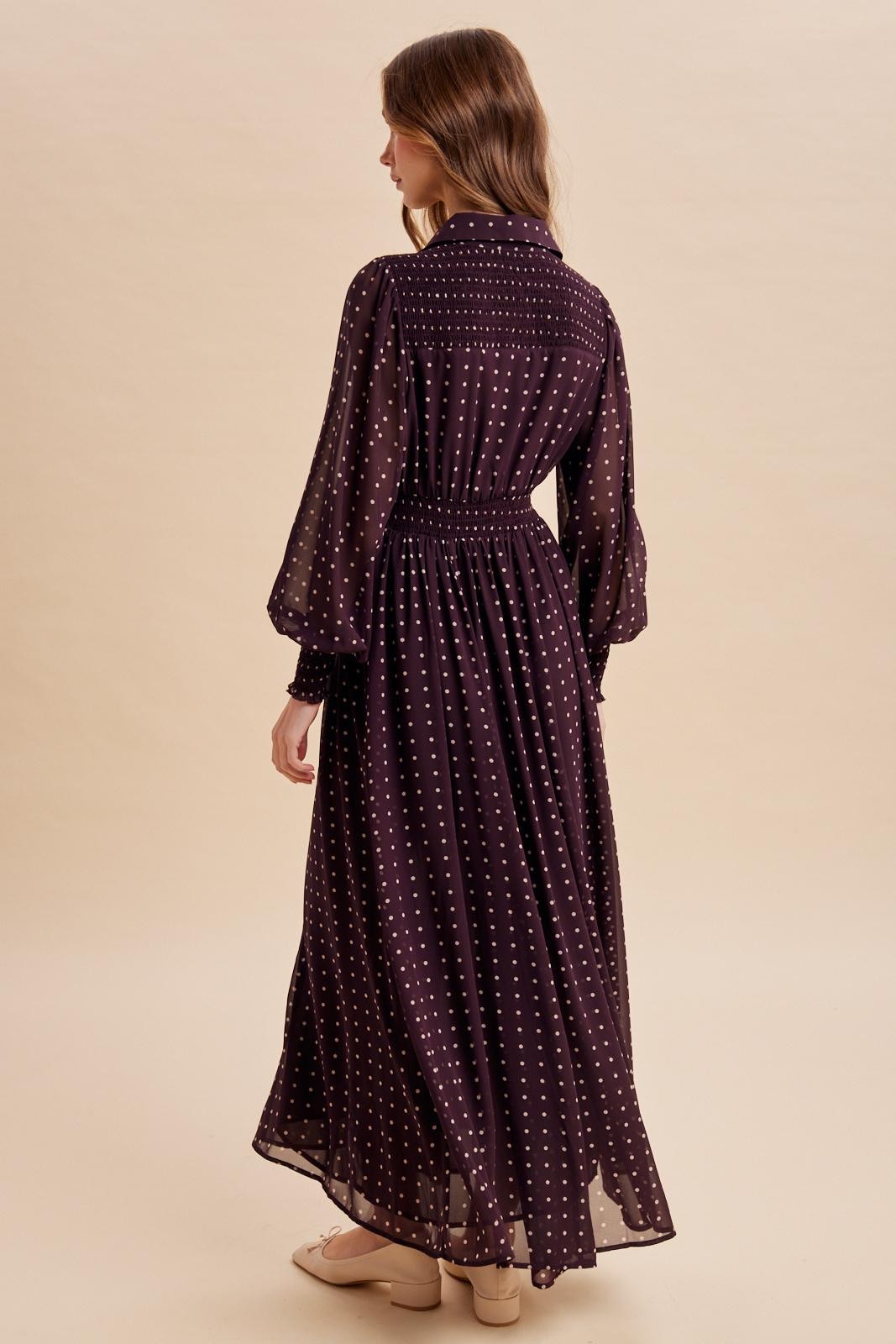 woman wearing a long purple polka dot dress with bell sleeves and a cinched waist, viewed from the back