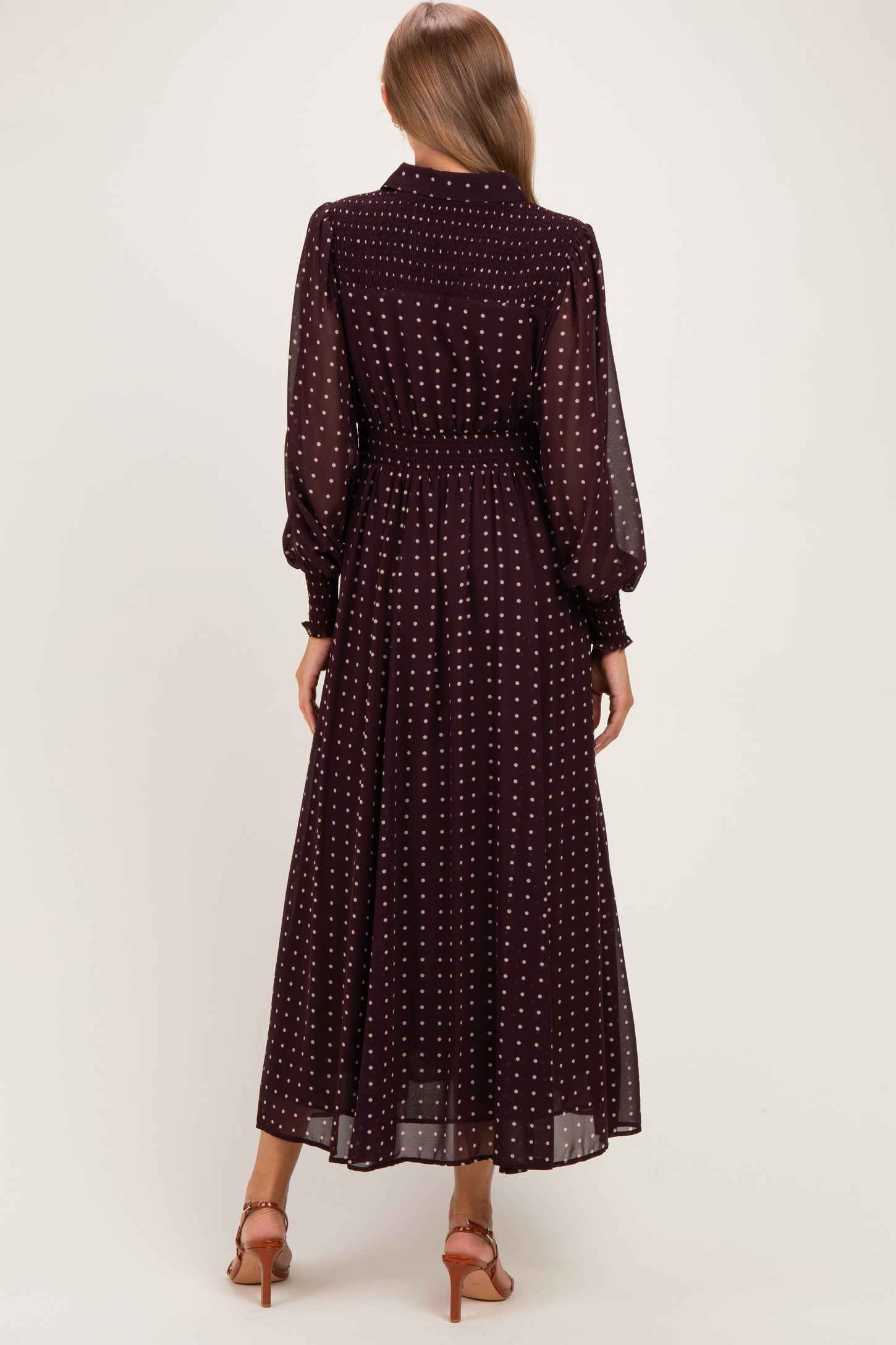 woman wearing a burgundy long sleeve maternity dress with white polka dots, showing the back view and a flowing skirt