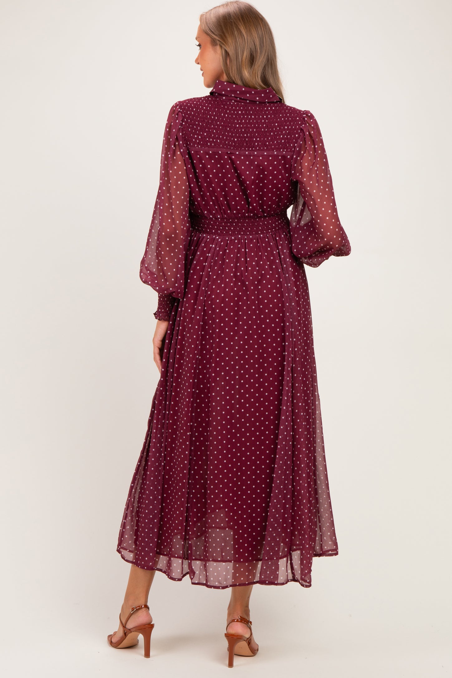 woman wearing a burgundy polka dot maternity dress with long sheer sleeves and a cinched waist, seen from the back