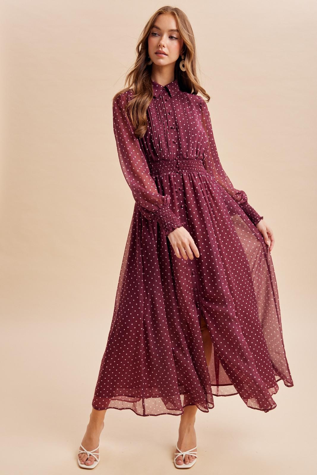 woman wearing a burgundy long sleeve maxi dress with white polka dots and a cinched waist, styled with white heeled sandals
