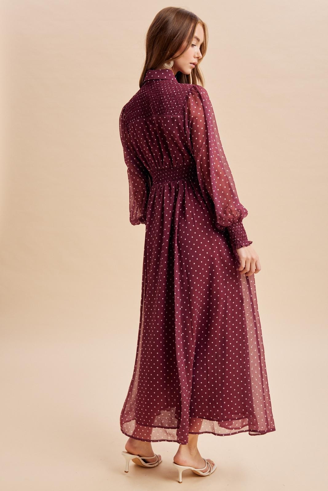 woman wearing a burgundy polka dot long sleeve maxi dress with a cinched waist and flowing skirt