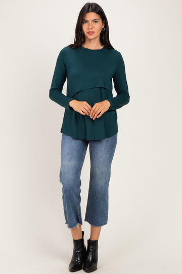 woman wearing a dark green long sleeve top with a tiered design and blue cropped jeans