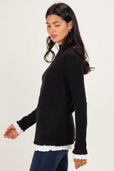 woman wearing a black ribbed long sleeve top with white ruffle details on the cuffs and hem