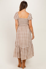 woman wearing a brown and white checkered maternity dress with puff sleeves and a tiered skirt, showing a baby bump