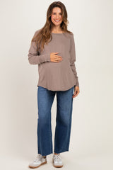 woman wearing a brown long sleeve maternity top and light blue wide leg jeans, holding her baby bump
