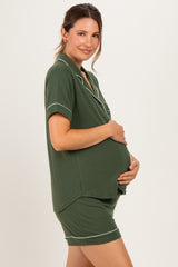 woman wearing a dark green maternity short pajama set, holding her baby bump