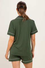 woman wearing a dark green maternity pajama set with short sleeves and contrasting white piping