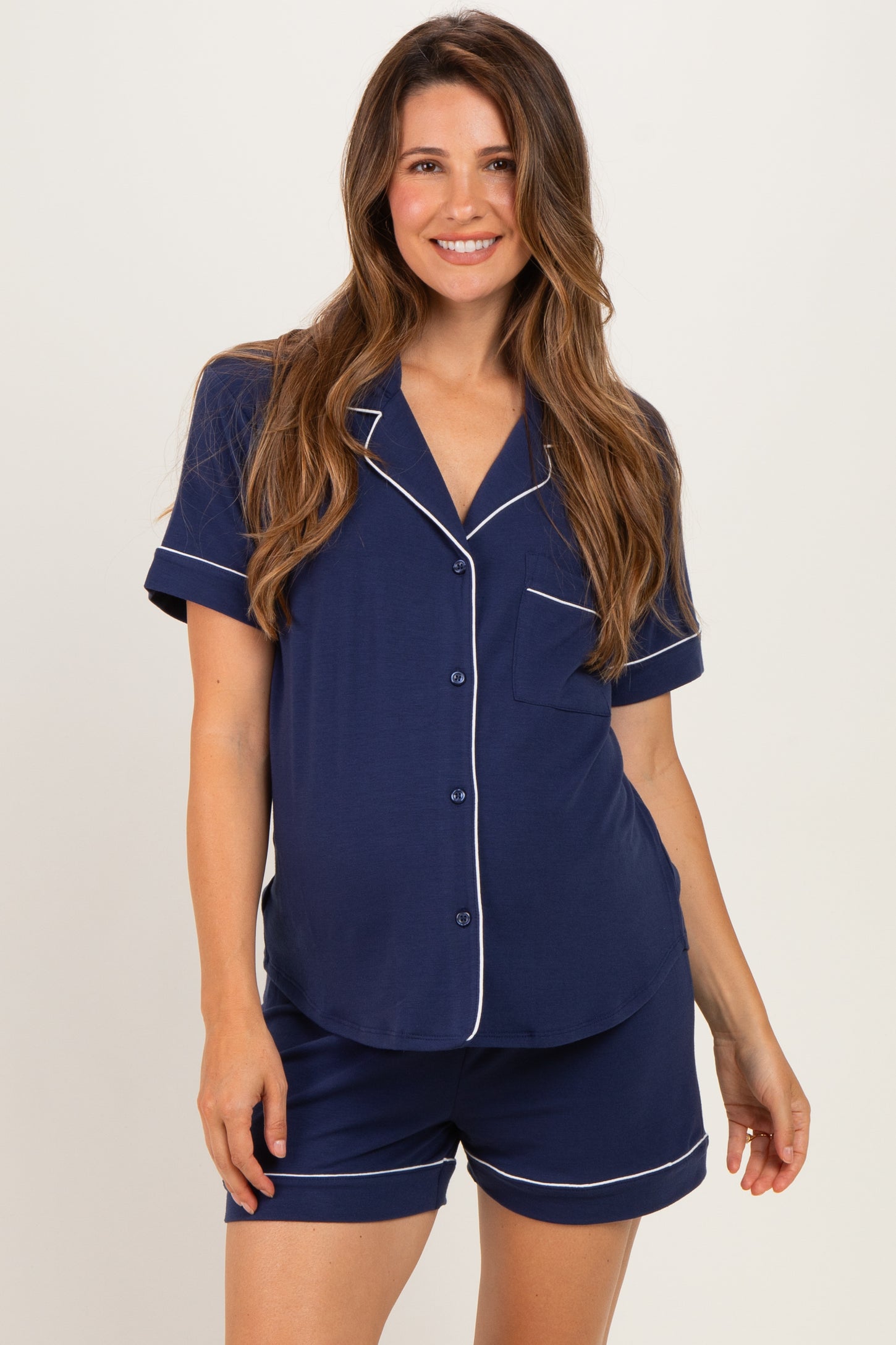 woman wearing a navy blue short sleeve maternity pajama set with white piping and a visible baby bump