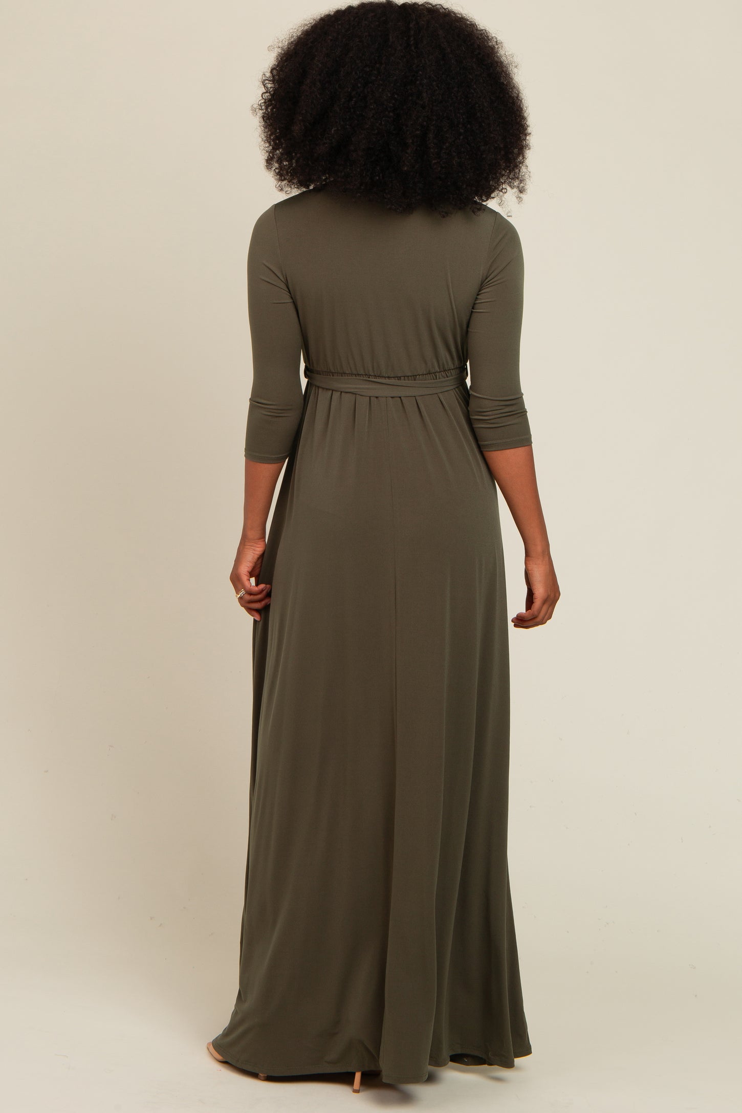 woman wearing a long olive green maxi dress with three-quarter sleeves and a cinched waist, viewed from the back