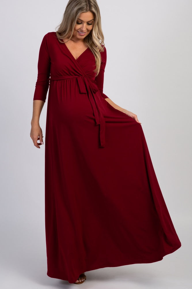 woman wearing a burgundy maternity maxi dress with a wrap design and three-quarter sleeves, showing a baby bump