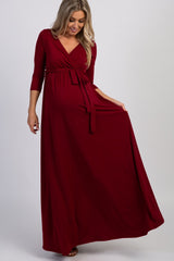 woman wearing a burgundy maternity maxi dress with a wrap design and three-quarter sleeves, showing a baby bump