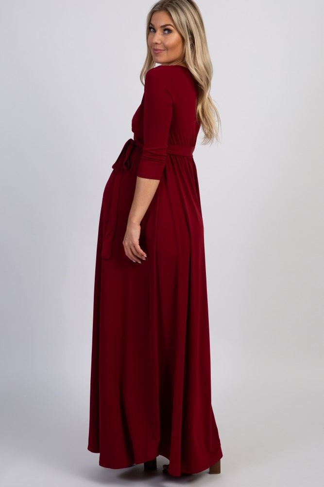 woman wearing a burgundy long sleeve maxi dress with a tied waist and a visible baby bump