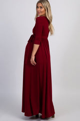woman wearing a burgundy long sleeve maxi dress with a tied waist and a visible baby bump