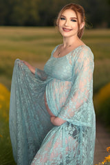 woman wearing a light blue lace maternity gown and holding her baby bump in a field setting
