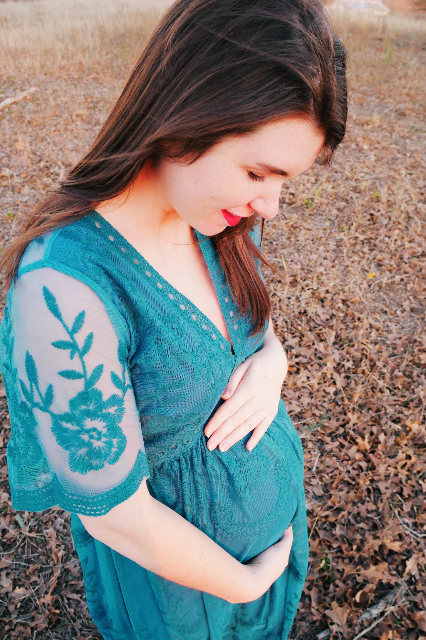 woman wearing a teal maternity dress with embroidered sleeves and cradling her baby bump