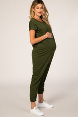 woman wearing a dark green maternity jumpsuit with a visible baby bump