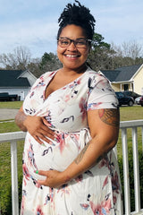 woman wearing a floral print maternity dress and holding her baby bump