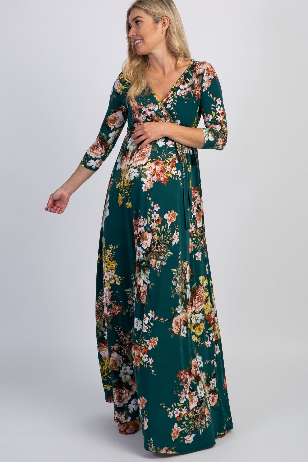 woman wearing a green floral maternity maxi dress with three-quarter sleeves and a visible baby bump
