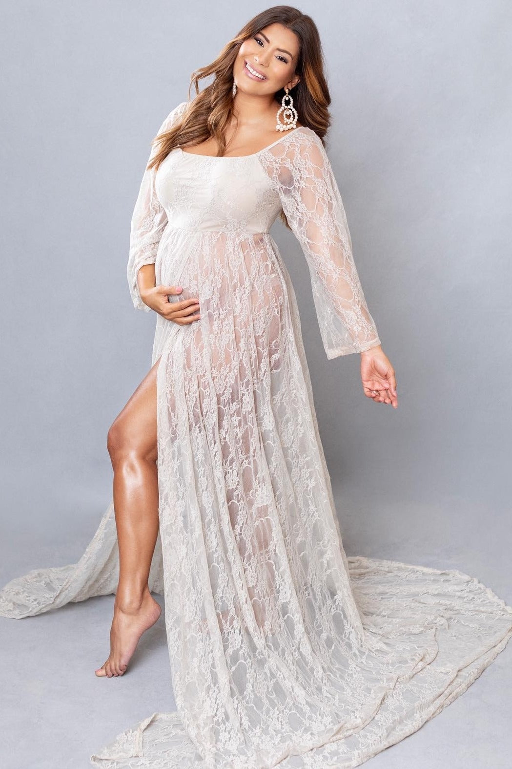 woman wearing a cream lace maternity gown with long sleeves and a thigh-high slit, showcasing her baby bump